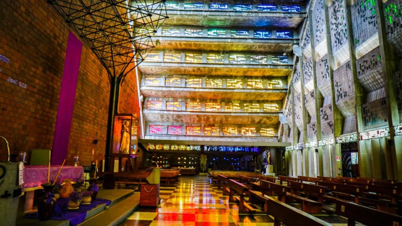 Interior de la Iglesia El Rosario con luz natural filtrándose en arcoíris a través de vitrales sobre la bóveda de concreto